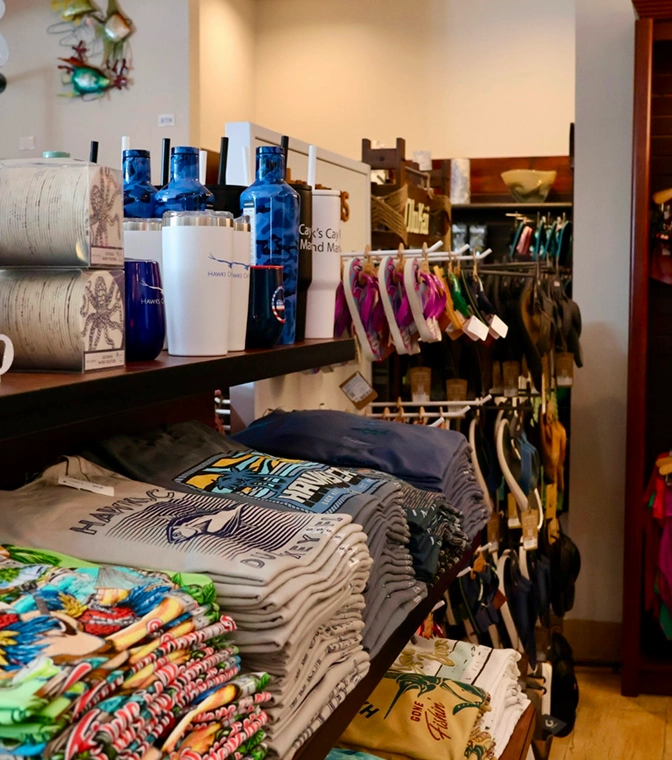 Resort gift shop featuring folded graphic t-shirts, branded tumblers, and colorful flip-flops on display shelves.