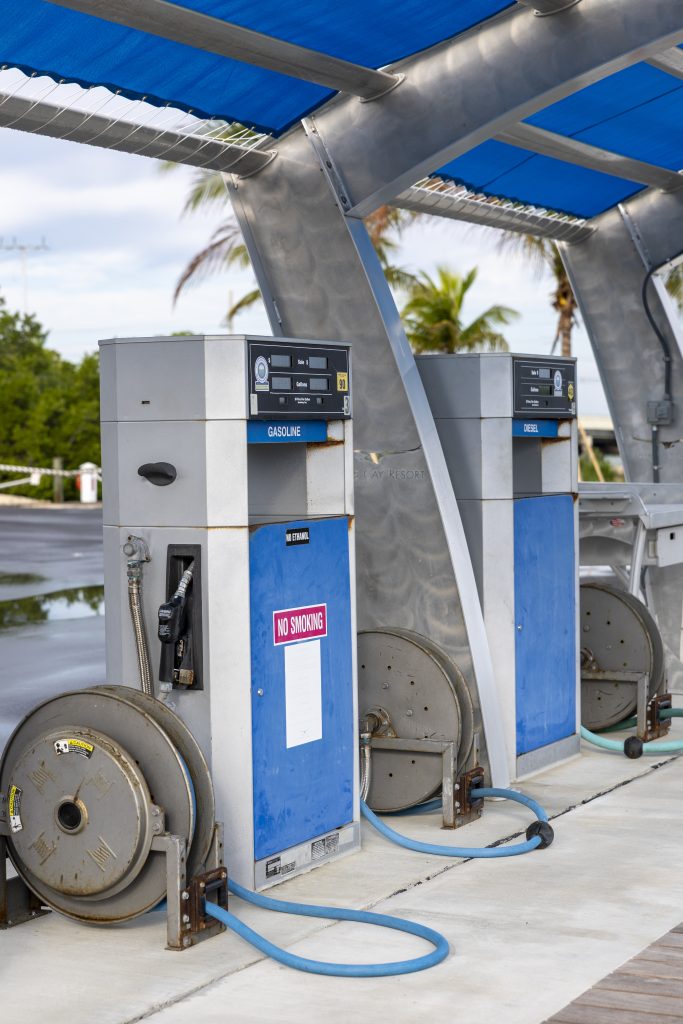 Gasoline and diesel fuel pumps with blue hoses under a covered marina fueling station.