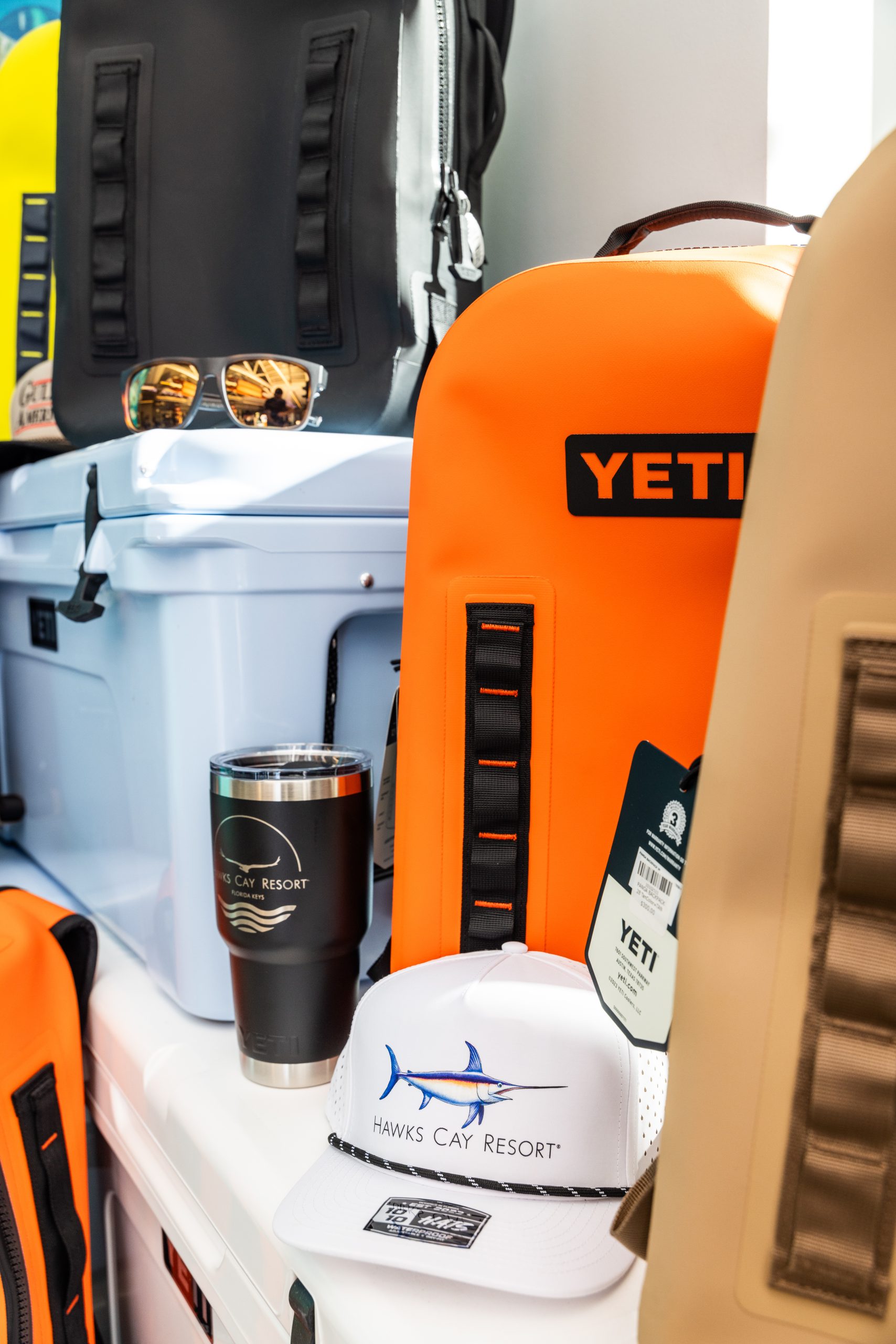 YETI outdoor gear display with orange backpack, cooler, tumbler, sunglasses, and Hawks Cay Resort hat.