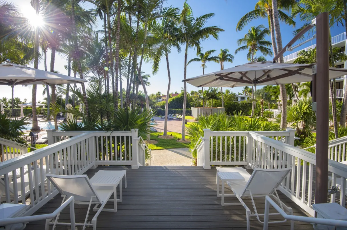 Sunlit wooden terrace at Hawks Cay Resort with white lounge chairs, umbrellas, and lush tropical palm trees.