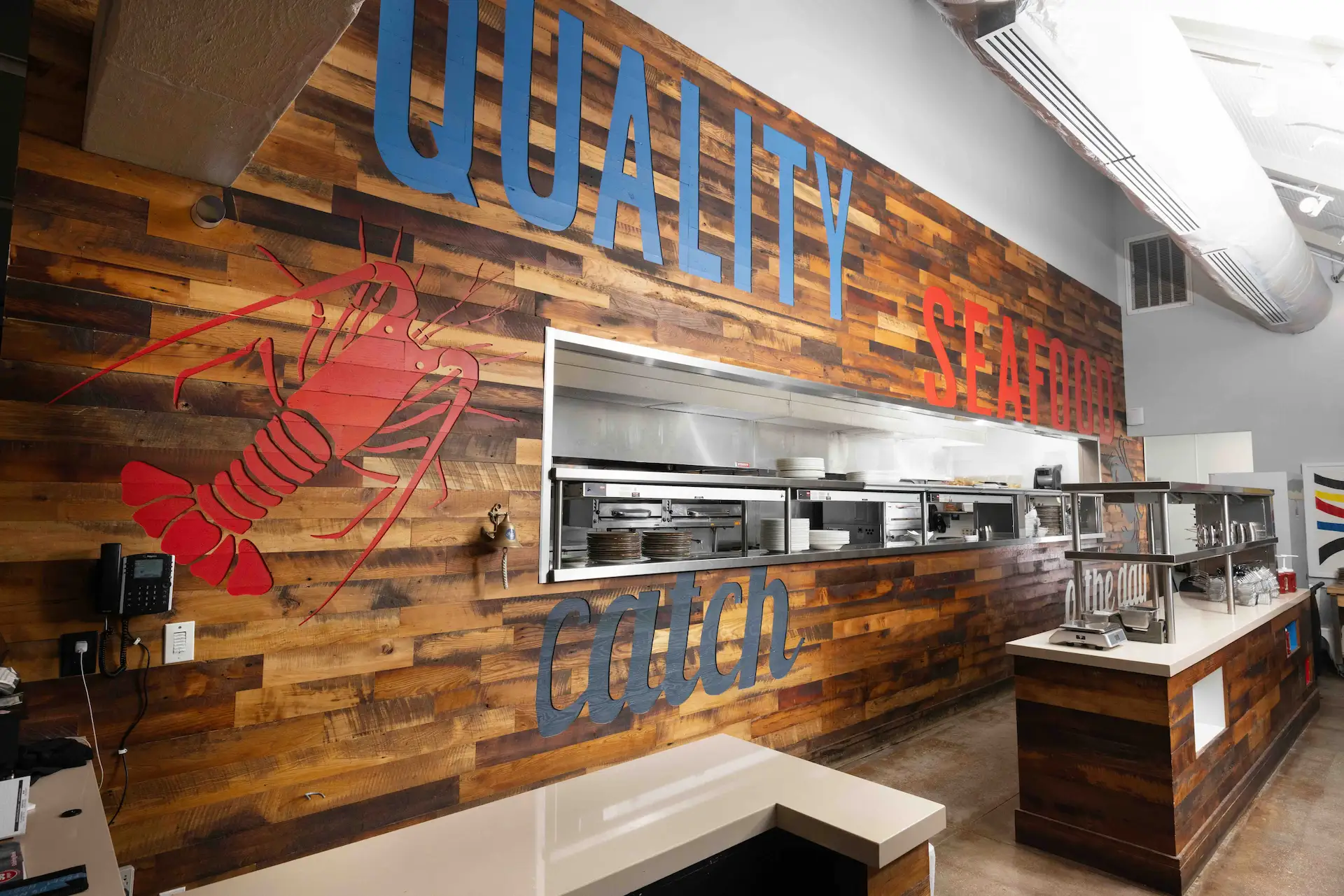 Rustic wood-paneled kitchen at Angler & Ale featuring a red lobster graphic and "Quality Seafood Catch" signage.