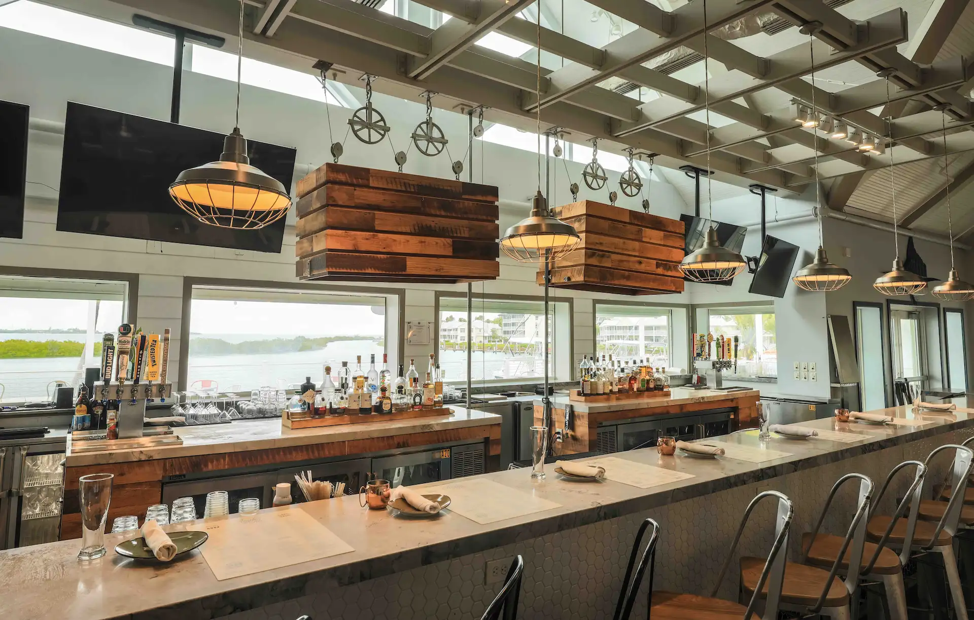 Modern indoor bar at Angler & Ale with marble counters, industrial pendant lights, and large windows with water views.