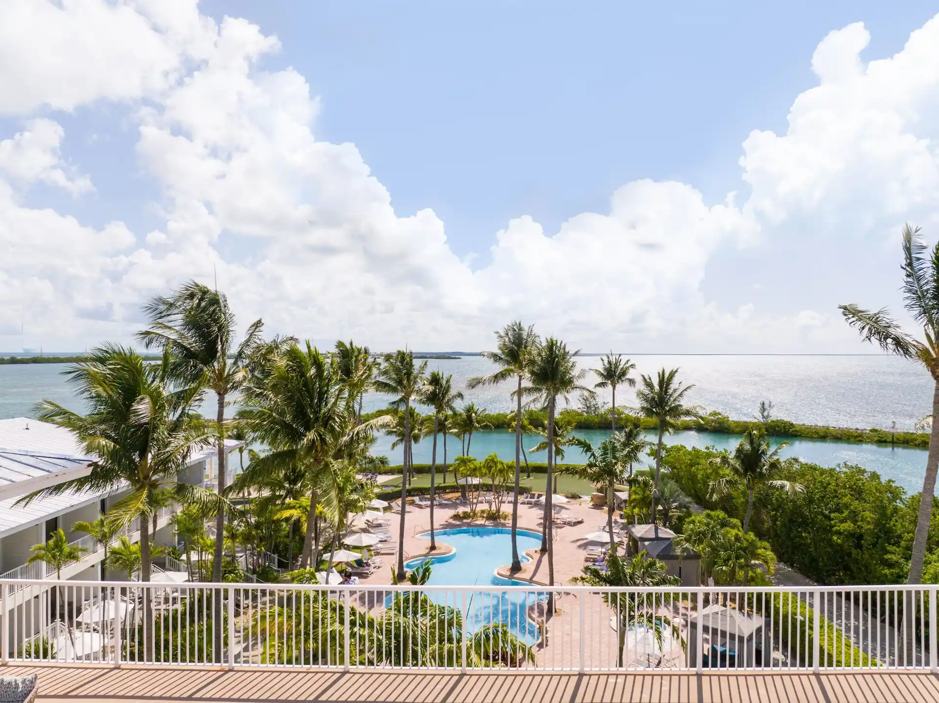 High-angle balcony view of the Hawks Cay resort pool, palm trees, and turquoise lagoon under a bright sky.