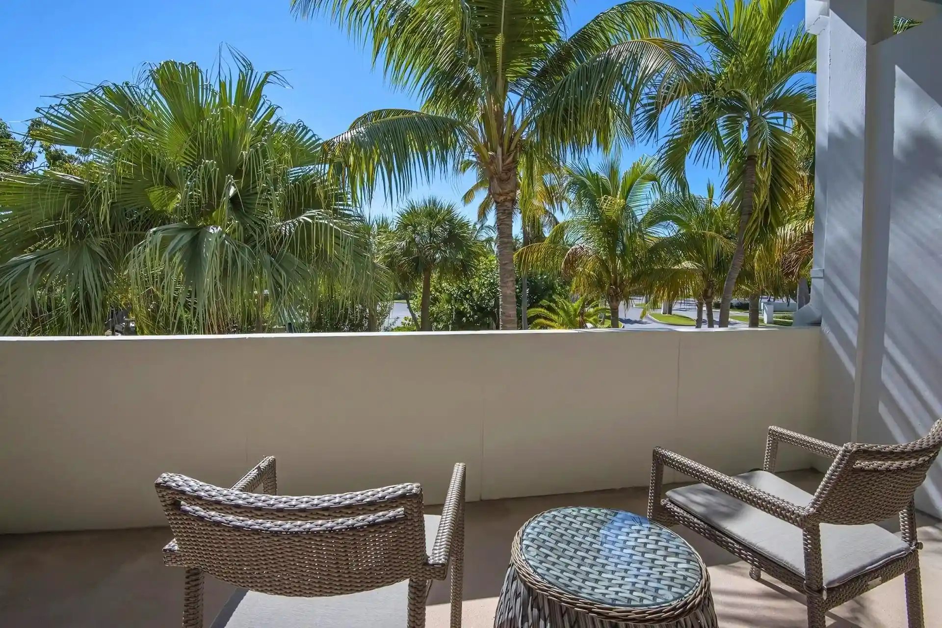 Wicker chairs and a glass table on a private Hawks Cay balcony overlooking lush tropical palm trees.