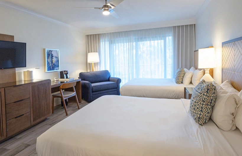 Modern Hawks Cay guest room with two queen beds, a blue armchair, and a wooden dresser and desk.