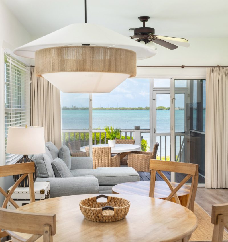A modern Hawks Cay villa living area with a wooden dining table and a glass door opening to a waterfront deck.