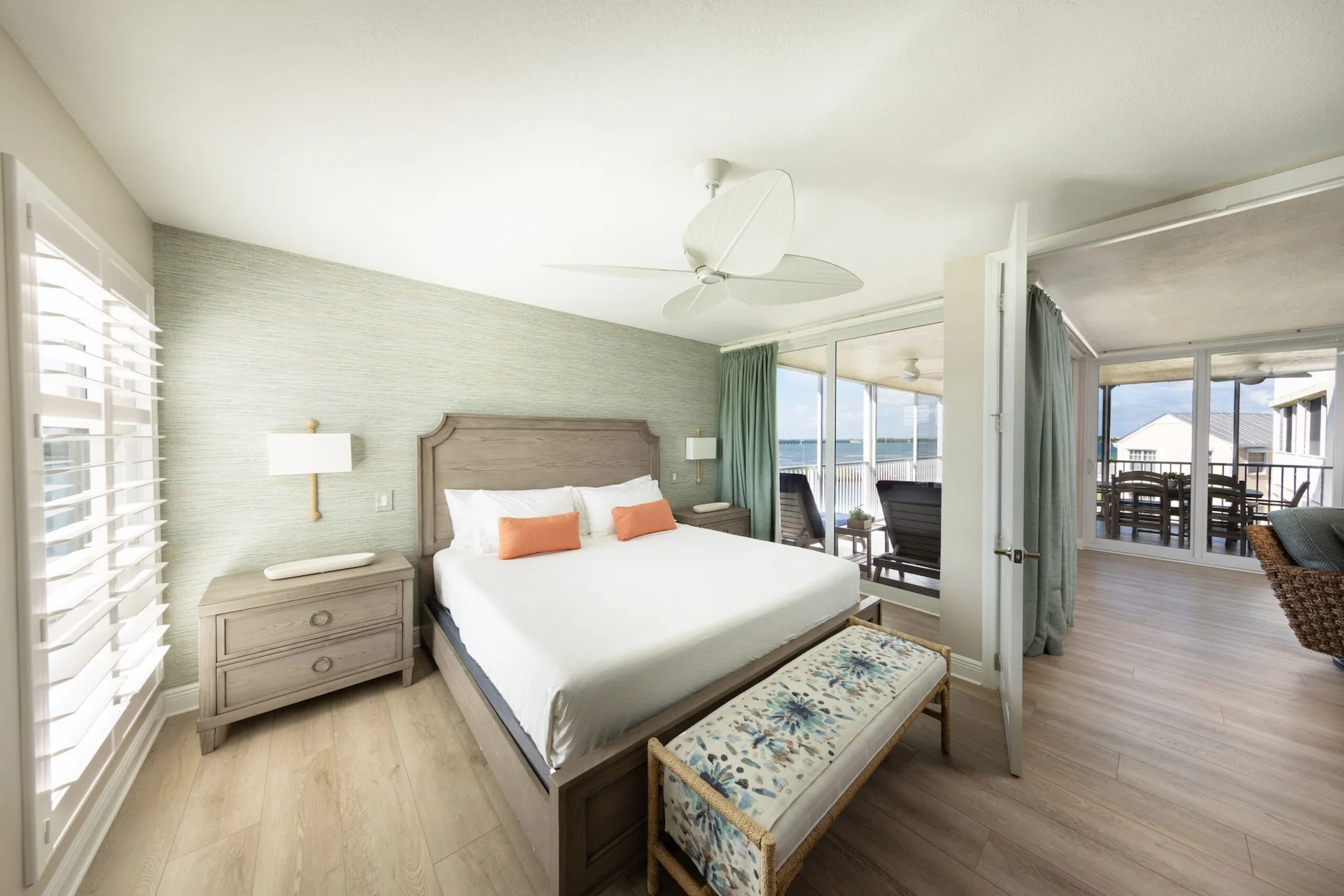 Modern bedroom with a king bed, wooden furniture, and glass doors opening to a balcony with ocean views.