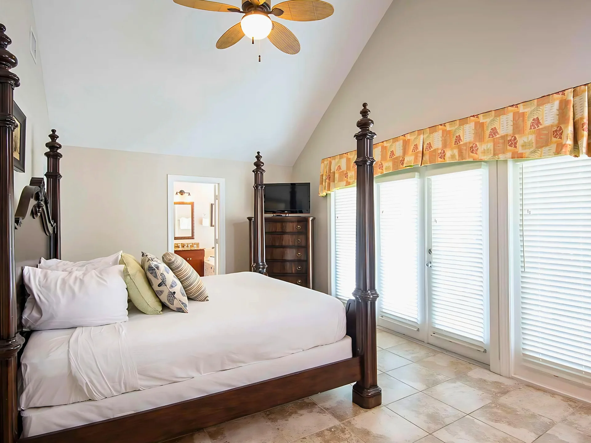 Traditional bedroom featuring a dark wood four-poster bed, vaulted ceiling, and white plantation shutters.