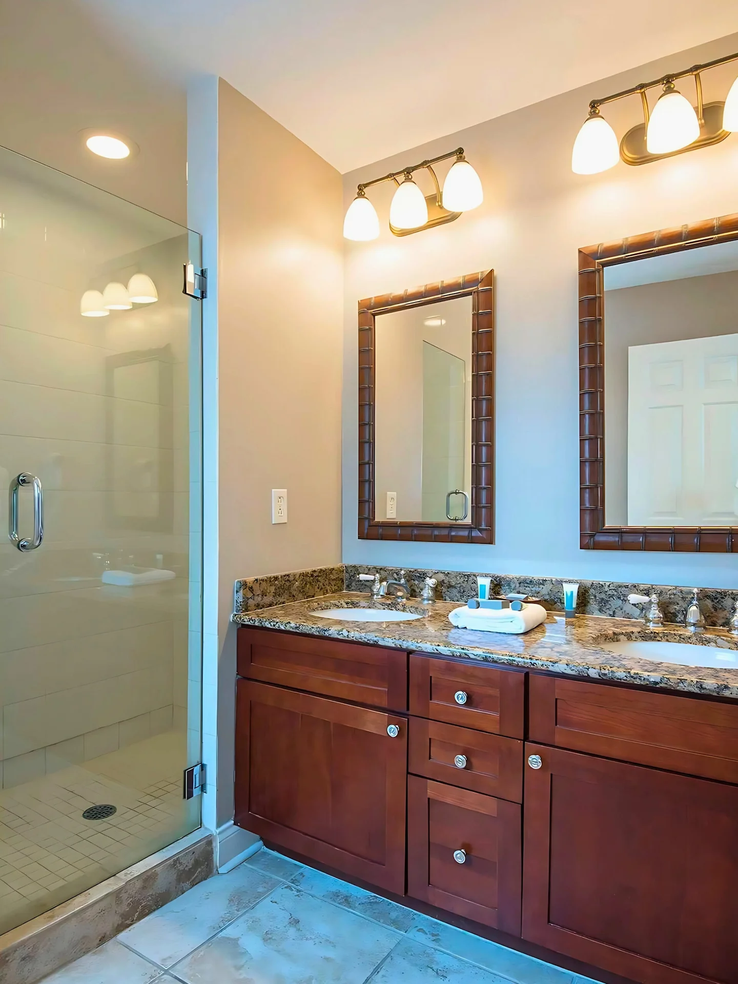 Modern bathroom featuring a double vanity with granite countertops and a walk-in glass shower.