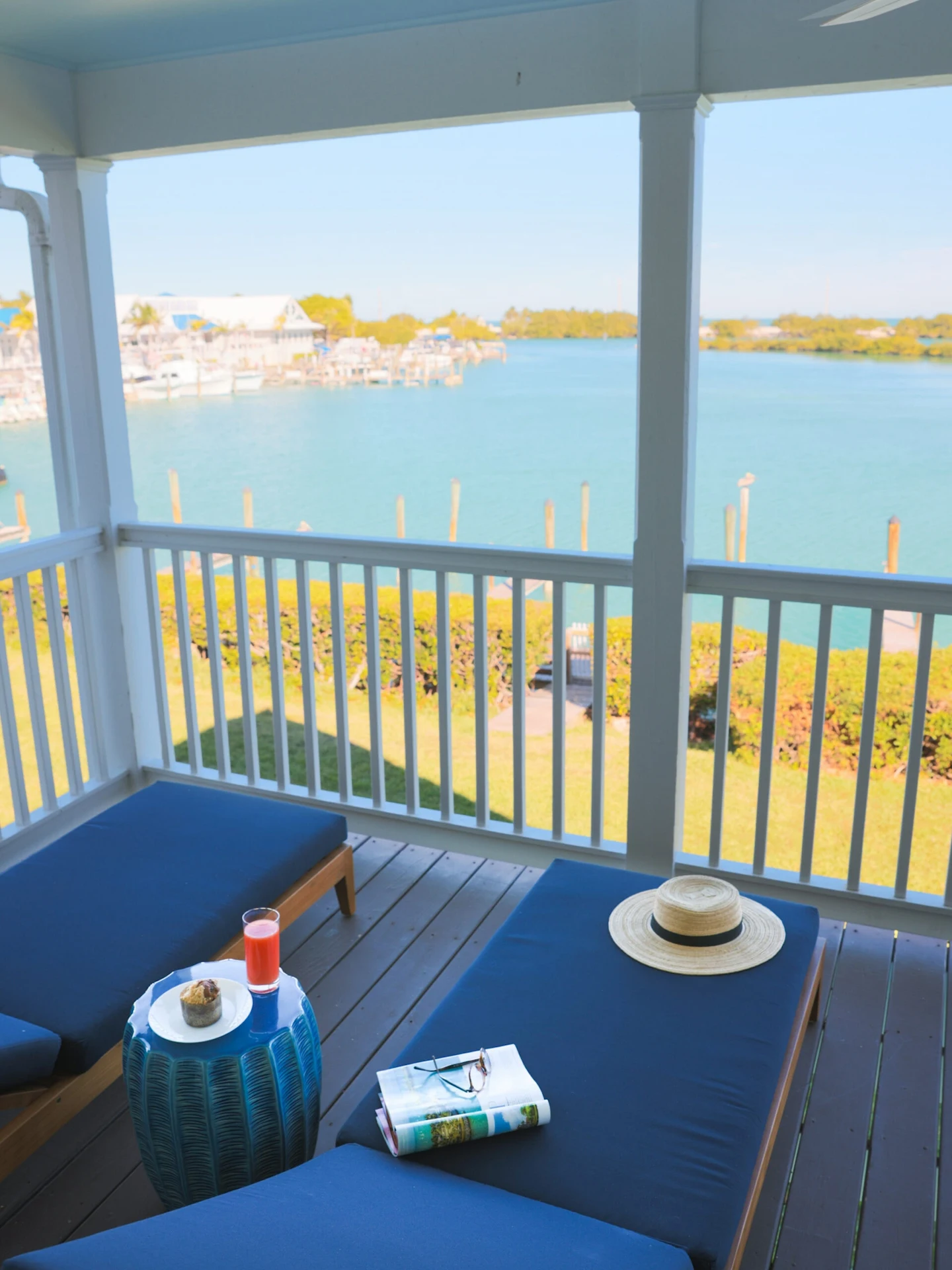 Two blue lounge chairs on a private wooden balcony overlooking a tropical canal and marina.