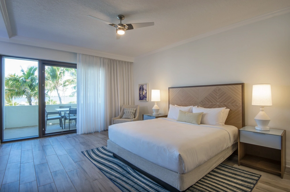 Modern junior suite with a king bed, striped rug, and sliding glass doors leading to a private furnished balcony.