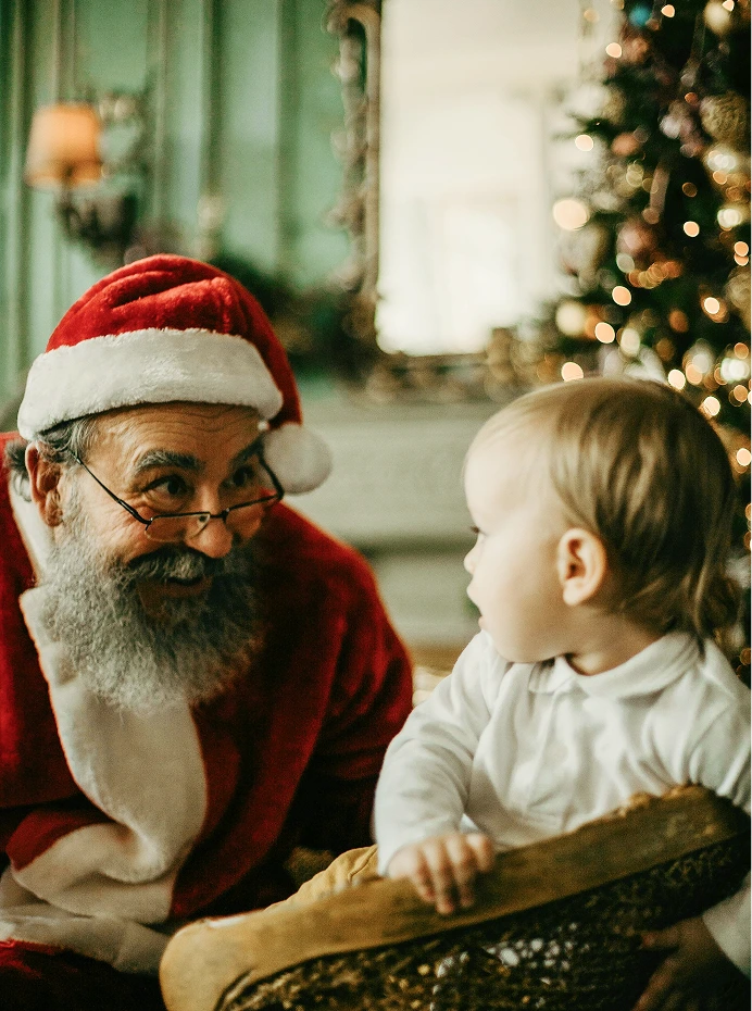 Santa Claus smiling at a young child in front of a blurred Christmas tree at a Hawks Cay holiday event.