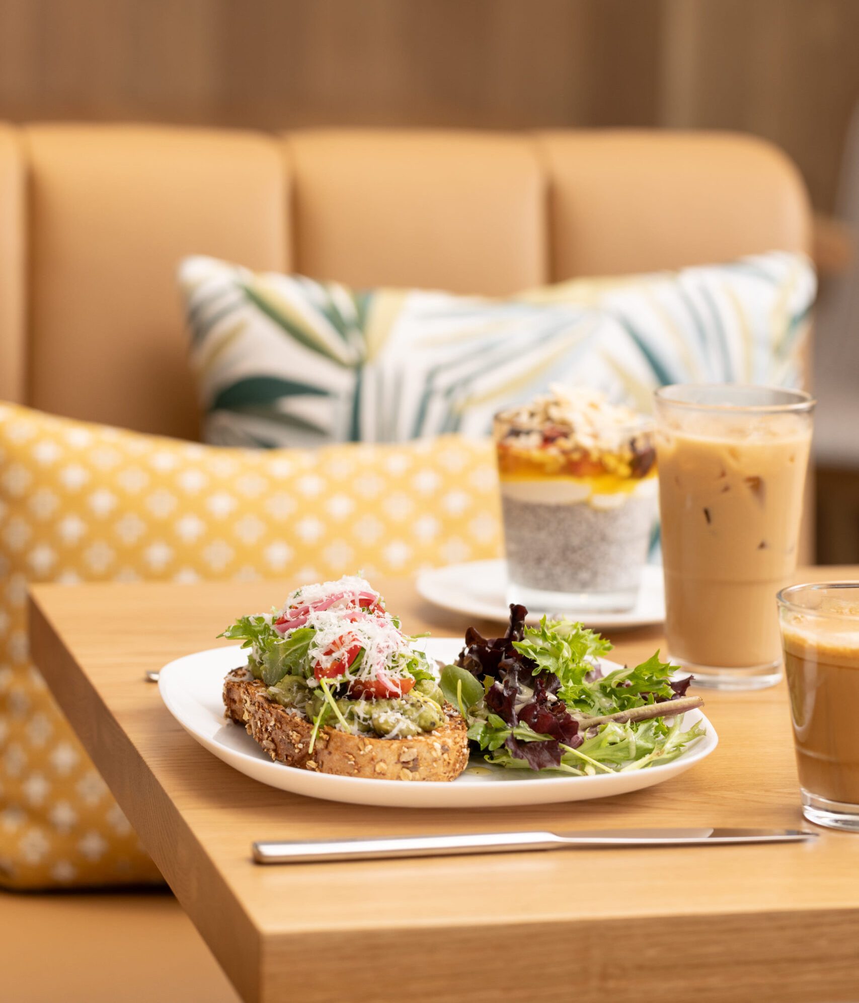 Avocado toast with greens and salad on a café table, served with iced coffee drinks in a cozy, modern setting.