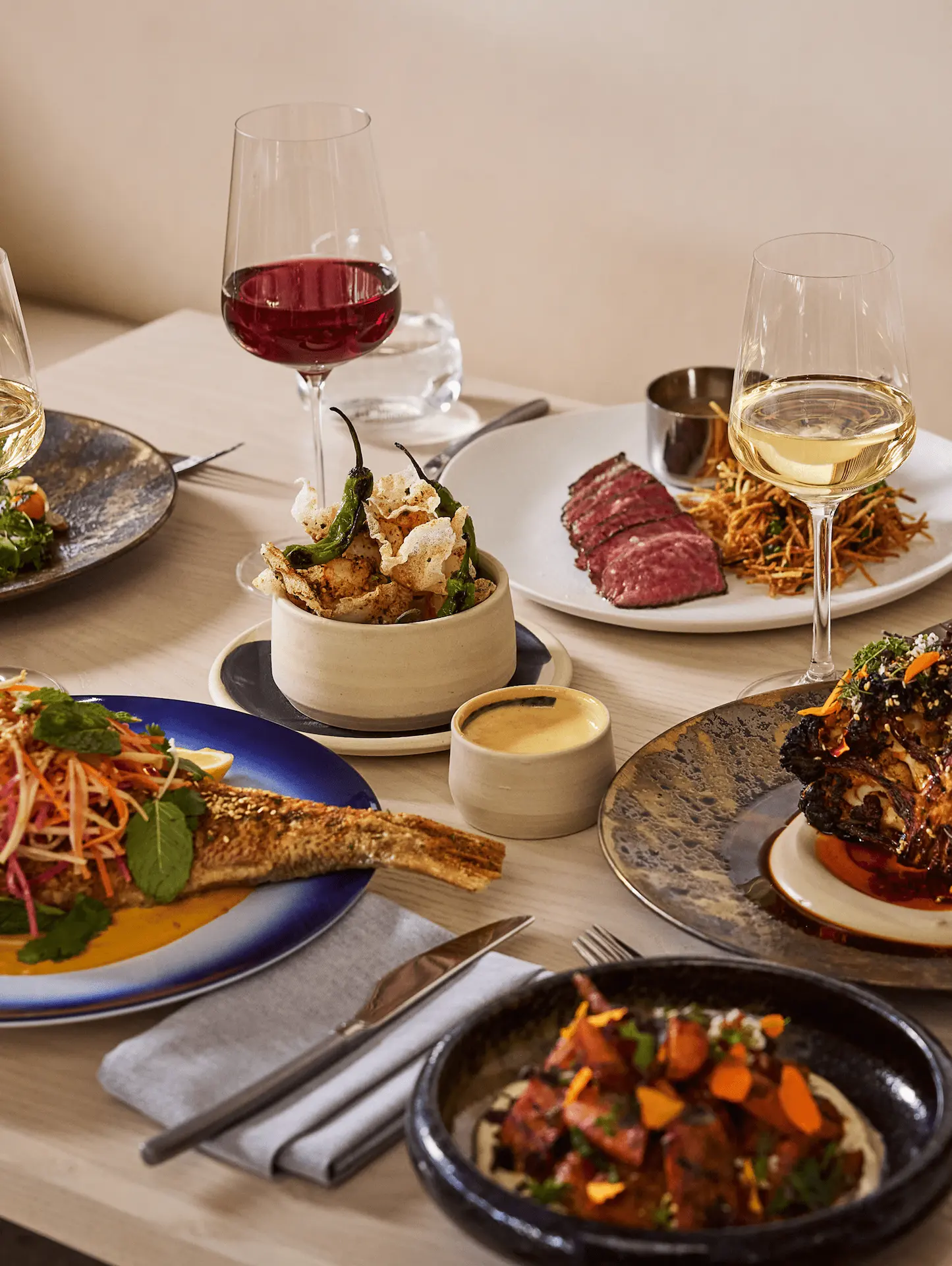 Gourmet dinner spread at Hawks Cay featuring sliced steak, whole fish, appetizers, and glasses of red and white wine.