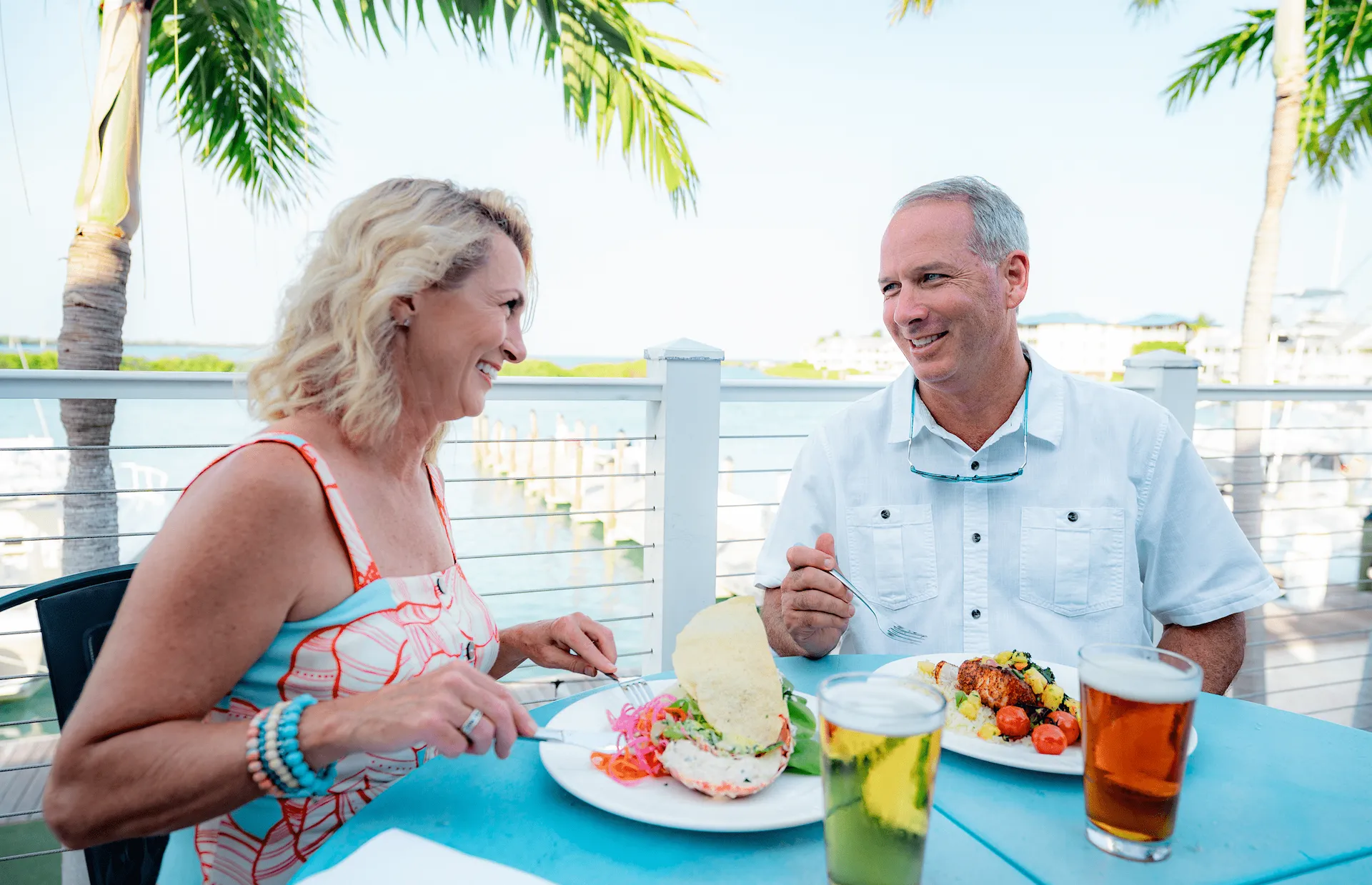 Couple smiling while enjoying a fresh seafood meal and beers at an outdoor waterfront table at Hawks Cay Resort.
