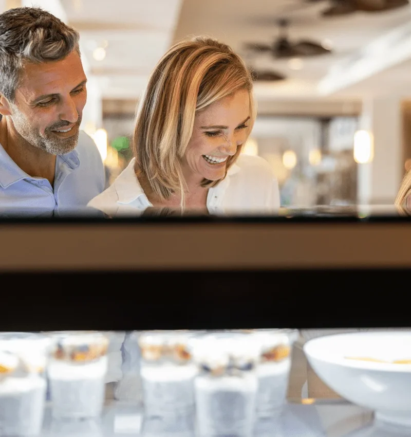 A smiling couple and their child looking at a selection of yogurt parfaits and breakfast items at Hawks Cay.