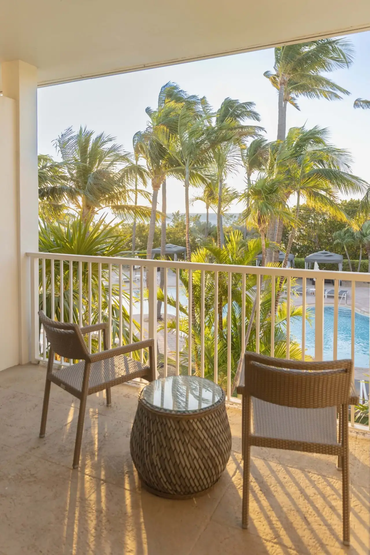 Sunset view from a Hawks Cay balcony with wicker chairs and a glass table overlooking palm trees and the pool.