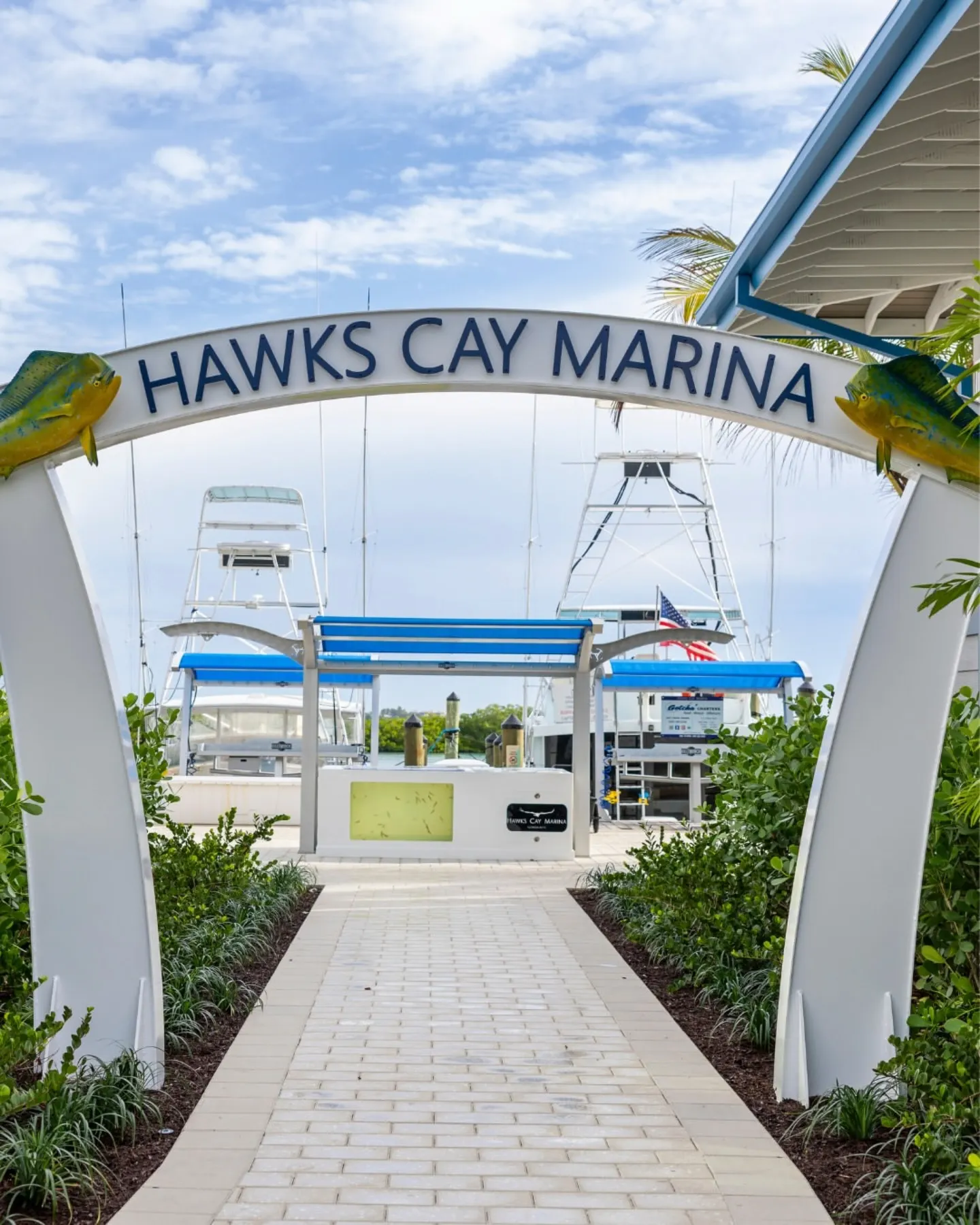 White "Hawks Cay Marina" arched entrance with yellow fish decor, leading to boat docks.