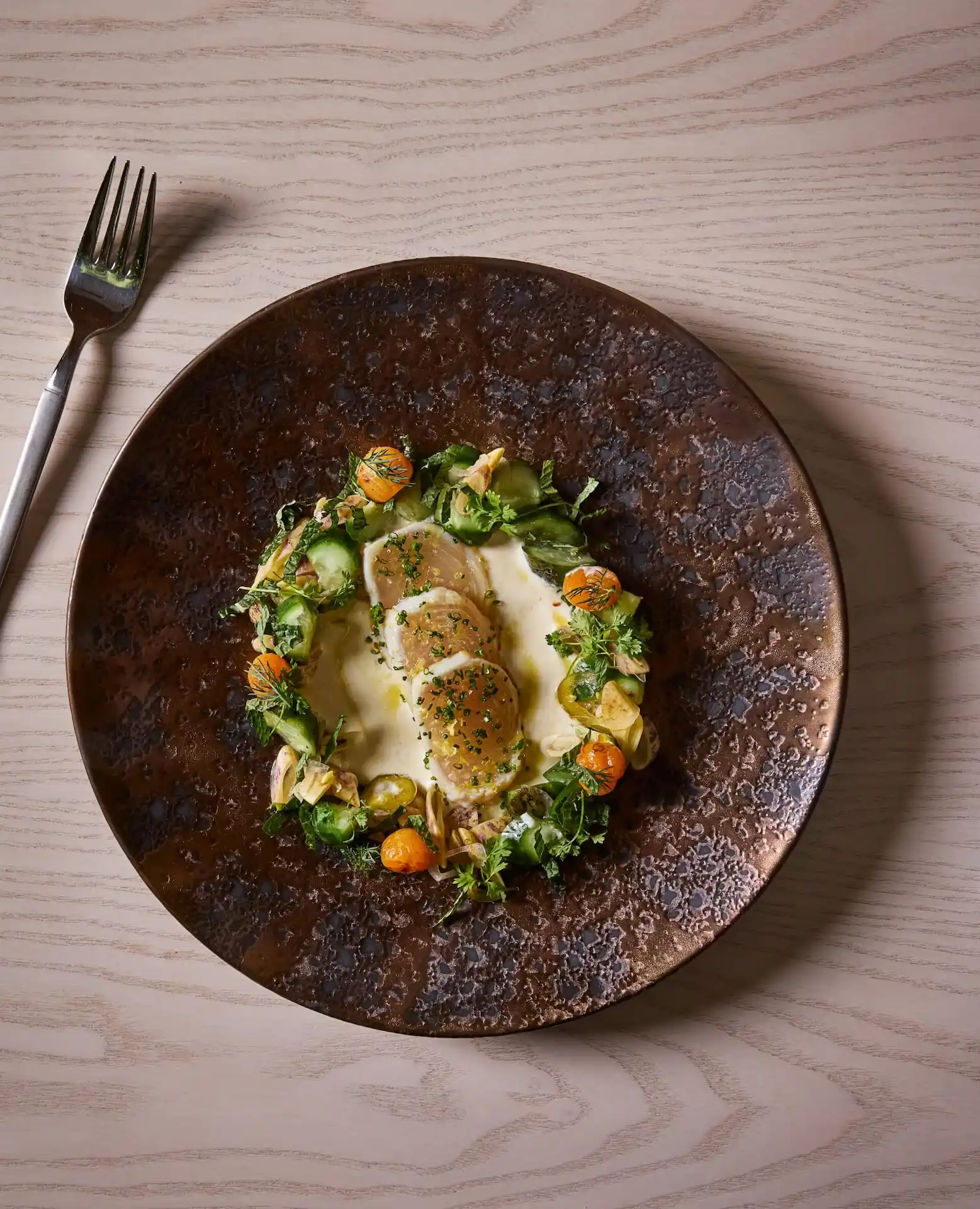 Plated gourmet dish with sliced scallops, creamy sauce, and fresh vegetables, served on a textured ceramic plate.