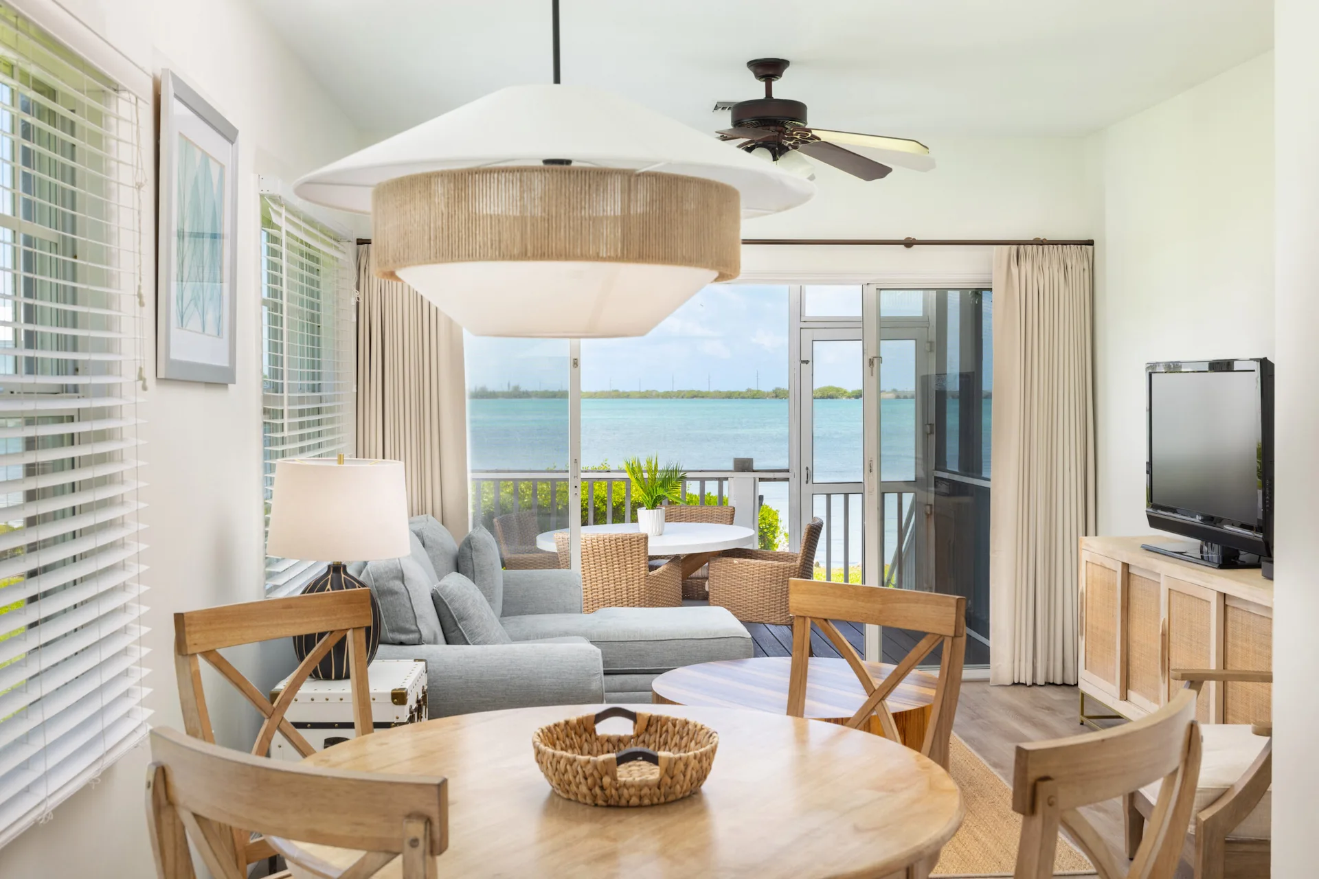 A modern Hawks Cay villa living area with a wooden dining table and a glass door opening to a waterfront deck.