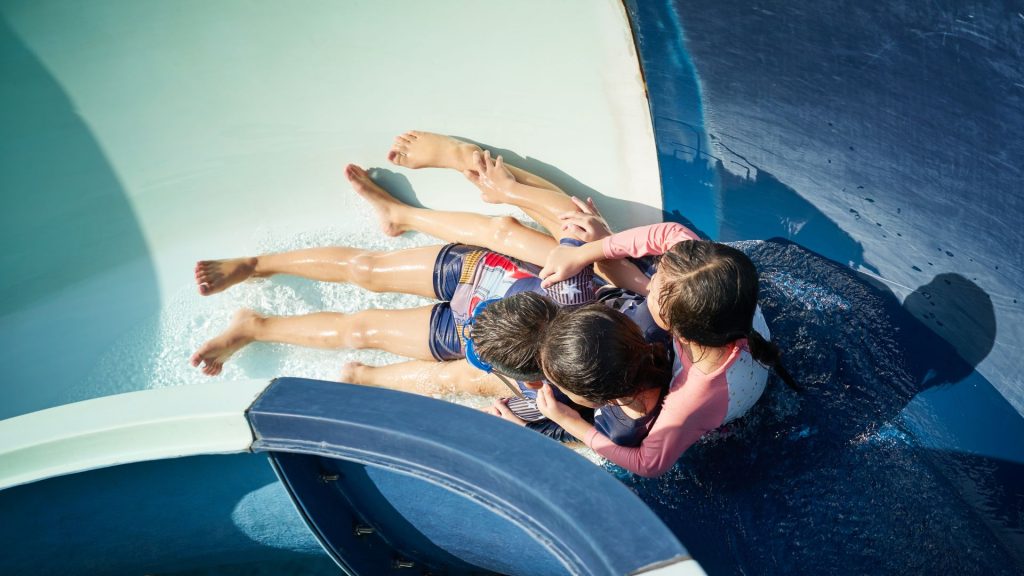 Three children race down a waterslide together at Coral Cay Adventure Park, splashing into the pool beneath the Florida Keys sun.