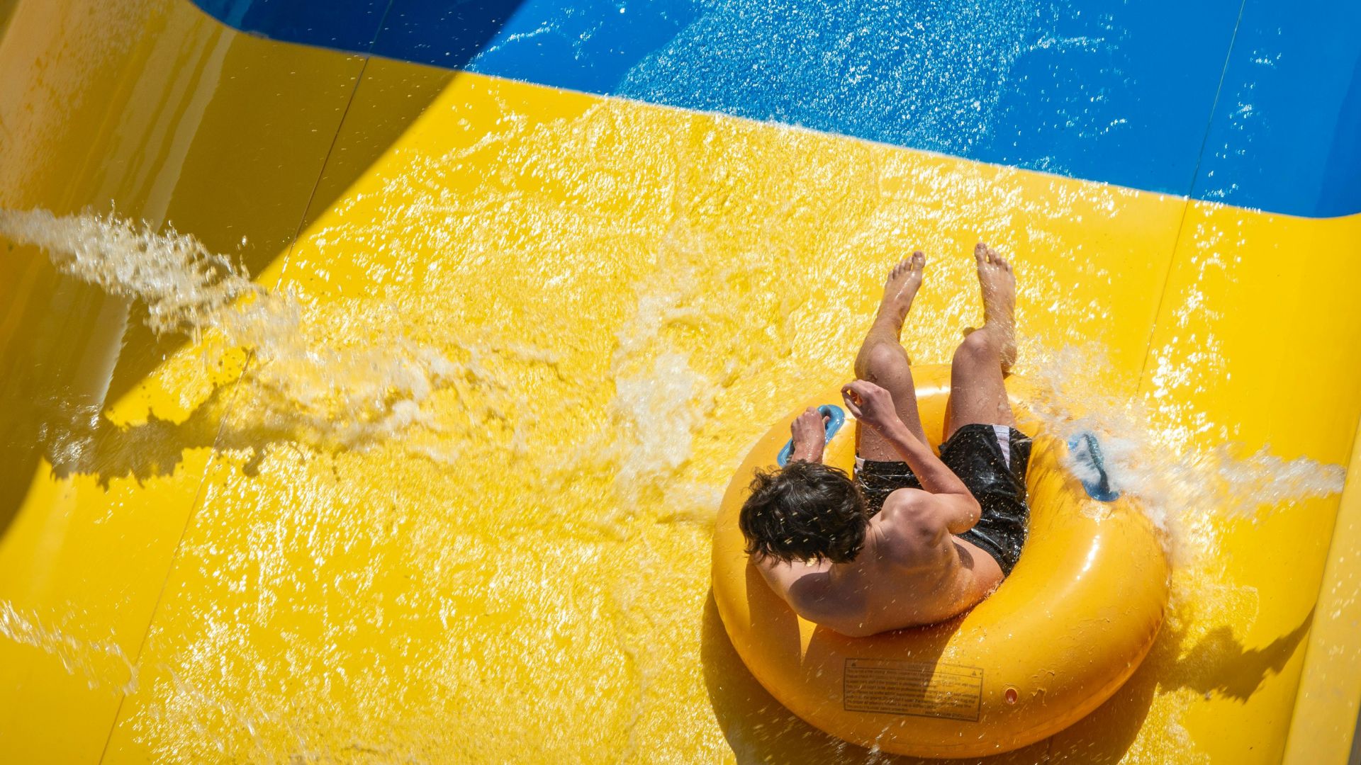 A guest rides a bright yellow inner tube down a waterslide at Coral Cay Adventure Park, splashing through sunlit water beneath the Florida Keys sky.